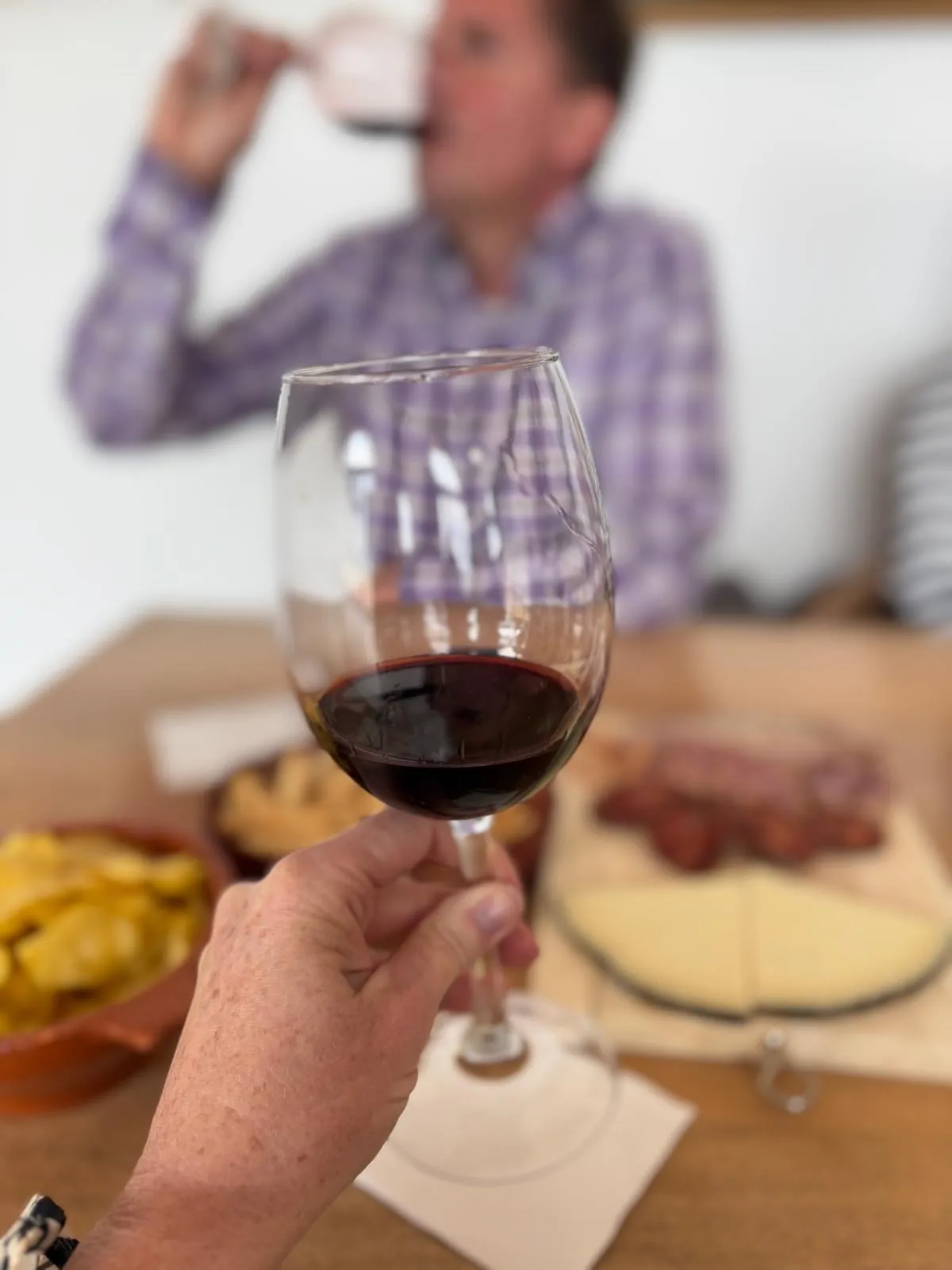 Een glas rode wijn wordt geproefd aan tafel, met Spaanse tapas — manchego, chorizo en olijfolie — op de achtergrond.